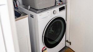Ein kleiner Waschraum mit Waschmaschine, Wäscheständer und einem an der Wand befestigten Feuerlöscher.