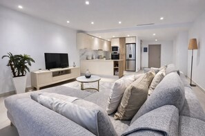 Moderni olohuone, jossa on sohva, sohvapöytä, televisio ja keittiöalue.