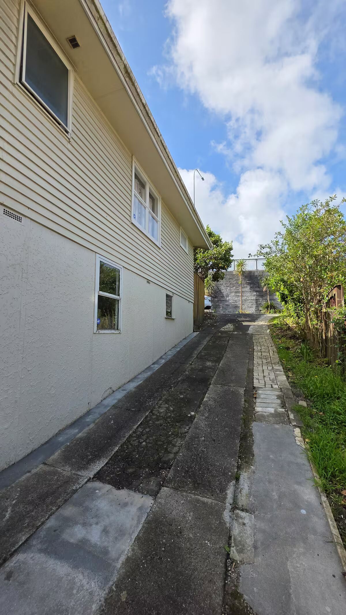 A narrow alleyway with a white building on one side and a tree-lined path on the other.
