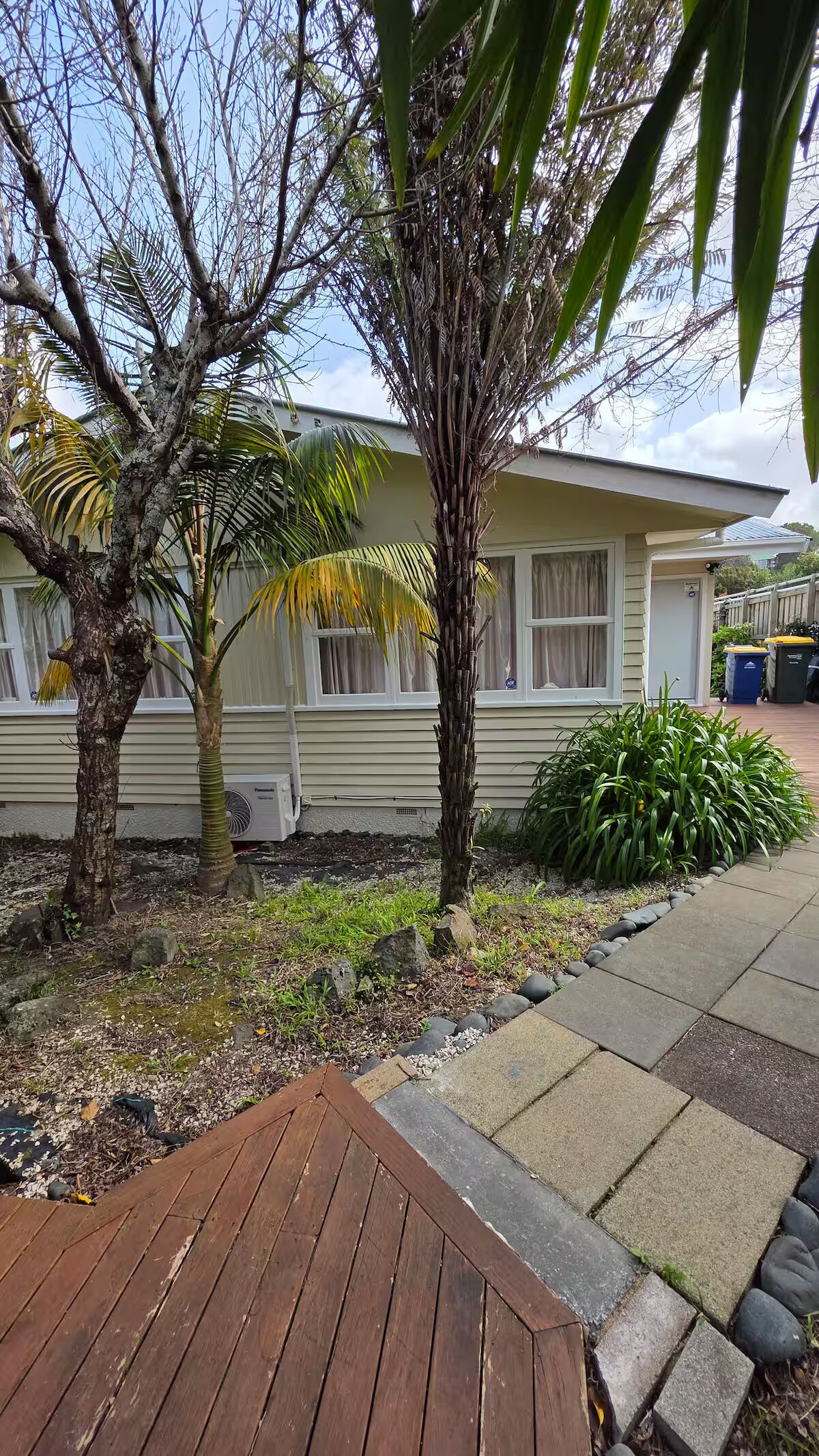 Een woonhuis met een houten terras, een palmboom en een beige gevel.