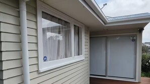 A house with a wooden deck, a window with a white blind, and a garage door. - Northshore Central Cosy & Comfortable 3BR Home (Auckland)
