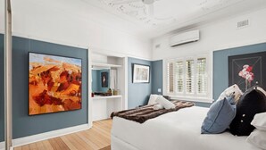 Un dormitorio con una cama, un cuadro abstracto grande y una ventana con contraventanas.