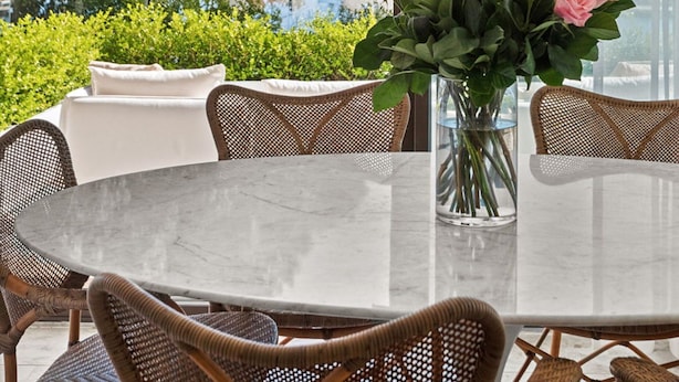 Un comedor con una mesa redonda, sillas de mimbre y un florero con flores rosadas.