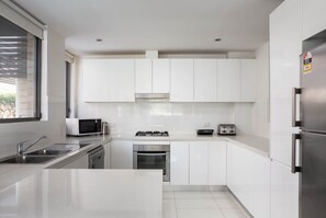 A modern kitchen with white cabinets, stainless steel appliances, and a large window. - Spacious Two-bedroom Apartment Near Hospital (Sydney)