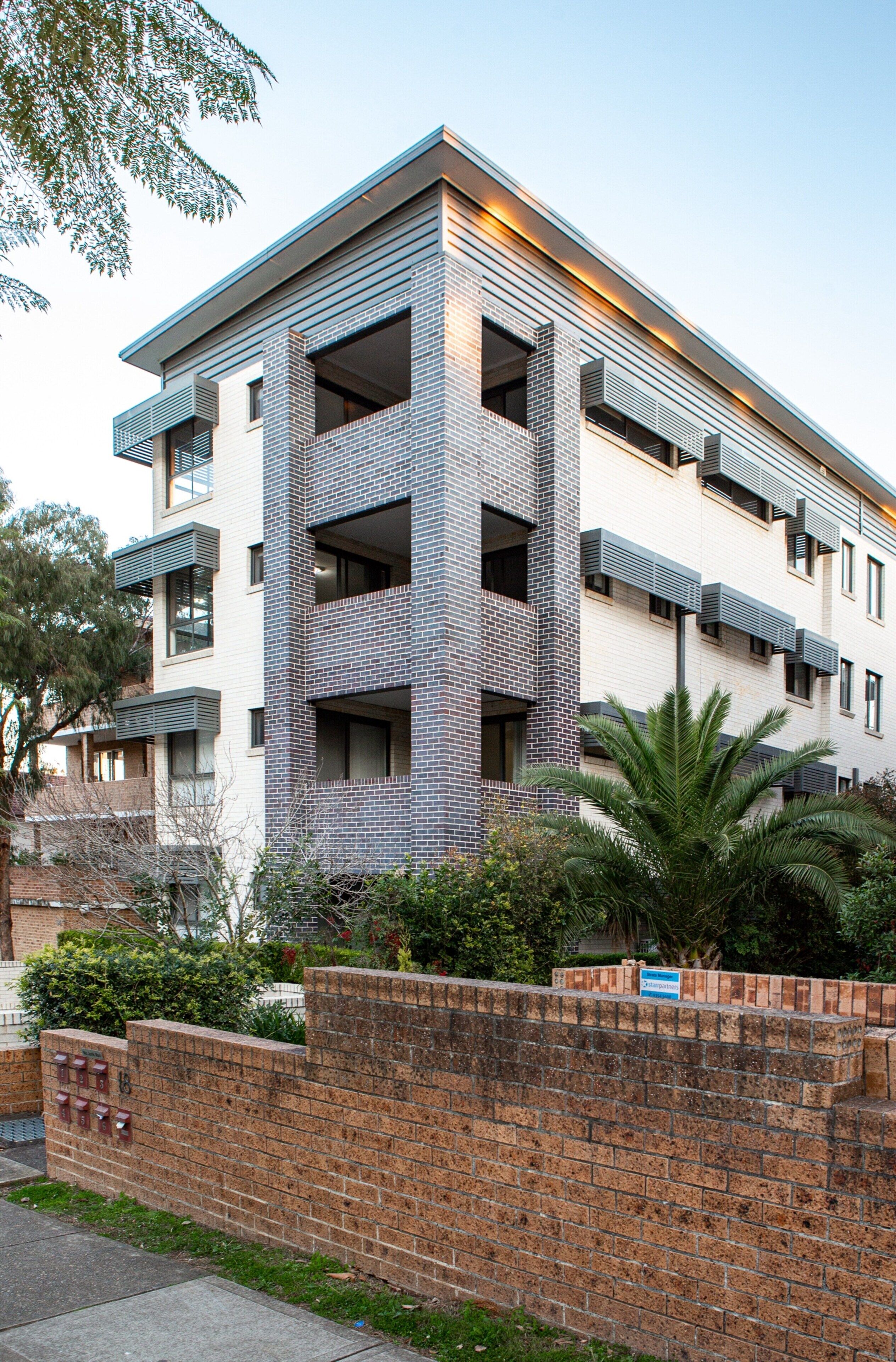 A multi-story building with a brick facade, balconies, and a brick wall in the foreground.