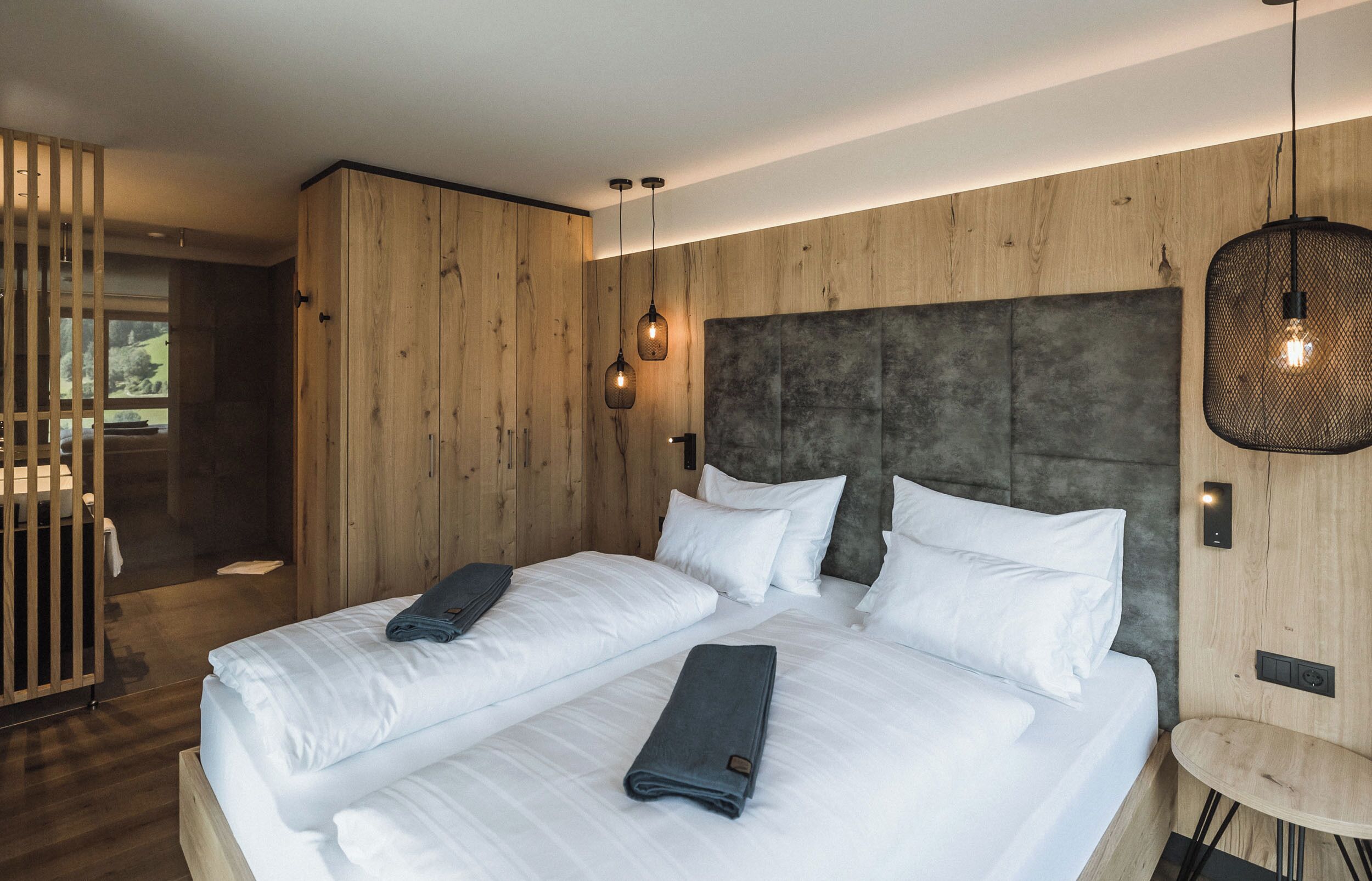 Une chambre d’hôtel moderne avec un grand lit, des murs recouverts de panneaux en bois et une petite table ronde.