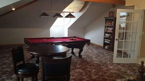 Une pièce avec une table de billard, des chaises, une bibliothèque et une porte.