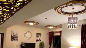 Una sala de estar con televisor, sofás rojos, una mesa de comedor con sillas y un techo decorativo.