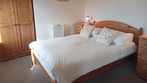 Een slaapkamer met een houten bed, witte beddengoed, een nachtkastje met lamp en een radiator.