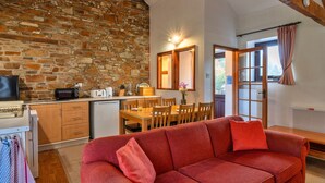 Una sala de estar acogedora con un sofá rojo, una pared de piedra, una mesa de comedor de madera y una zona de cocina con microondas y tostadora.