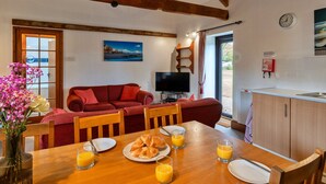 Una sala de estar acogedora con un sofá rojo, una mesa de comedor de madera con croissants y jugo de naranja, y un televisor.