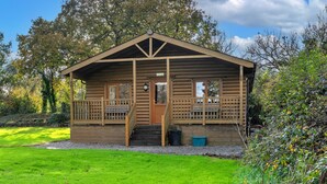 A wooden cabin with a porch, a front door, and a small staircase leading to the entrance. - Tarka's Holt Log Cabin, Stowford (Torrington)