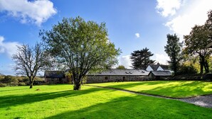 A stone building with a sloped roof, surrounded by a well-maintained lawn and trees. - Tarka's Holt Log Cabin, Stowford (Torrington)