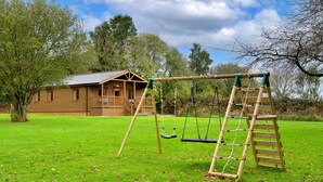 A wooden cabin with a swing set and a ladder in a grassy area. - Tarka's Holt Log Cabin, Stowford (Torrington)
