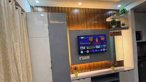 A modern living room with a flat-screen TV, ceiling fan, and built-in shelves. - Charming bed & breakfast in enchanting Greater Noida with AC (Greater Noida)