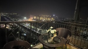 A balcony with wicker furniture and a vase of flowers, overlooking a cityscape at night. - Charming bed & breakfast in enchanting Greater Noida with AC (Greater Noida)