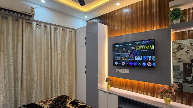 A modern bedroom with a bed, a ceiling fan, an air conditioner, a TV mounted on the wall, and a small plant on the shelf. - Charming bed & breakfast in enchanting Greater Noida with AC (Greater Noida)