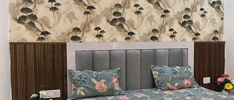 A bedroom with a floral-patterned headboard, a grey upholstered bed, and a bedside table with a vase of flowers.