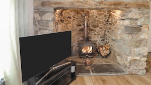Una llar de pedra amb un foc a llenya modern, un televisió de pantalla plana i una taula petita amb un aparell per escalfar aigua.