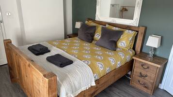 Un lit en bois avec une couvre-lit à motifs, deux oreillers, une table de chevet avec une lampe et un miroir au-dessus du lit.