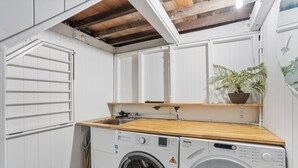 Une petite buanderie équipée de deux machines à laver à chargement frontal, d’un plan de travail en bois, d’un évier et d’une plante en pot.
