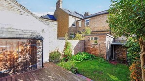 Un jardin arrière d’une maison, avec une terrasse en bois, des murs en briques et un petit espace aménagé en jardin.