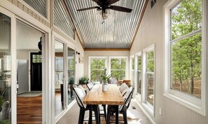 A dining area with a wooden table and chairs, large windows, and a ceiling fan.
