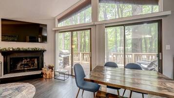 Una habitación amplia con una gran mesa de madera, una chimenea y vistas a una terraza y árboles.
