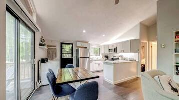 Una cocina moderna con armarios blancos, una isla central y un comedor con mesa de madera y sillas azules.