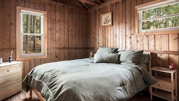 A wooden cabin bedroom with a bed, two nightstands, a dresser, and two windows.