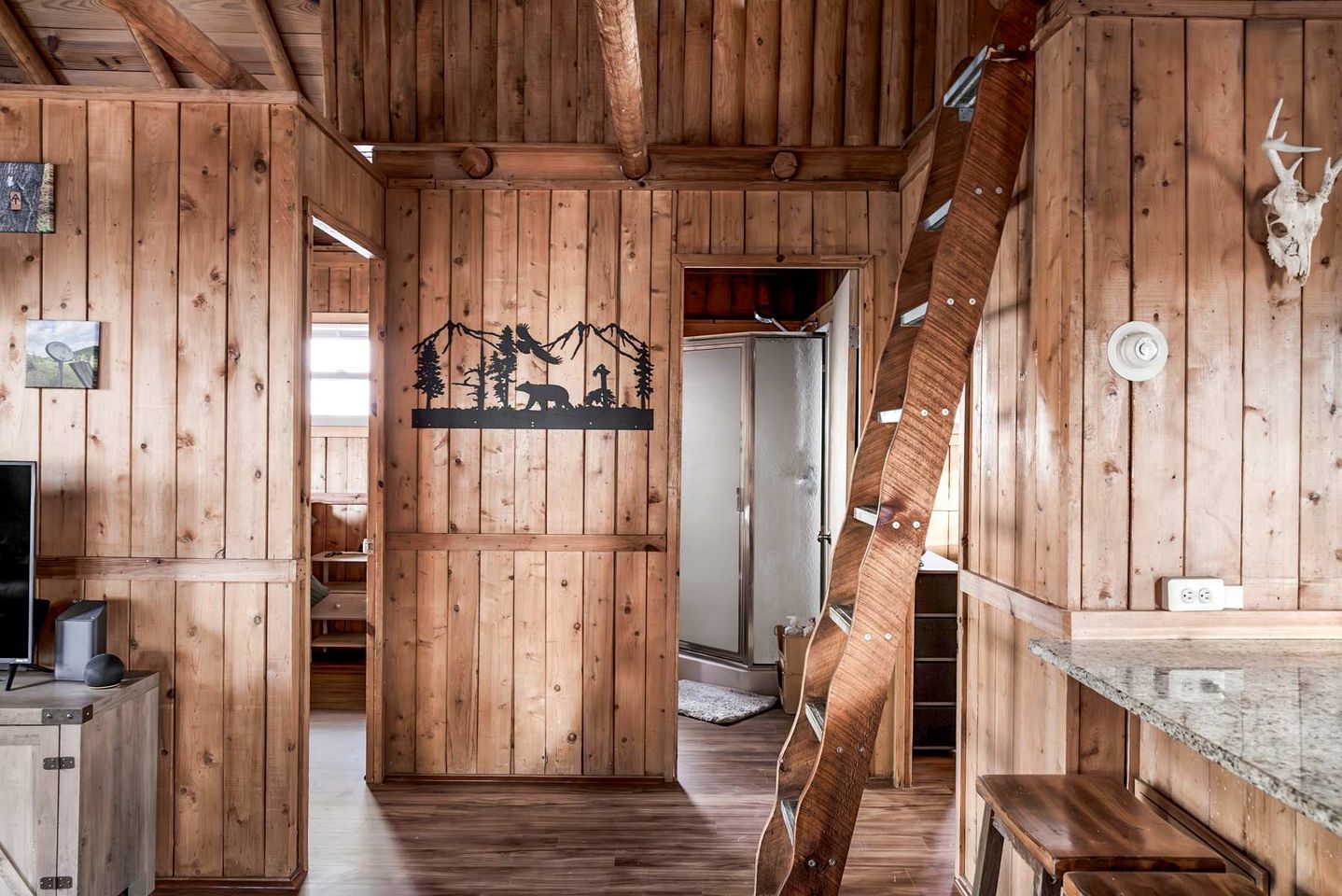 A wooden interior with a central hallway, a mounted animal skull, and a silhouette artwork.