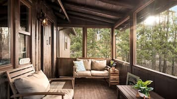 A wooden cabin with a porch, a sofa, a bench, and a table with a plant.