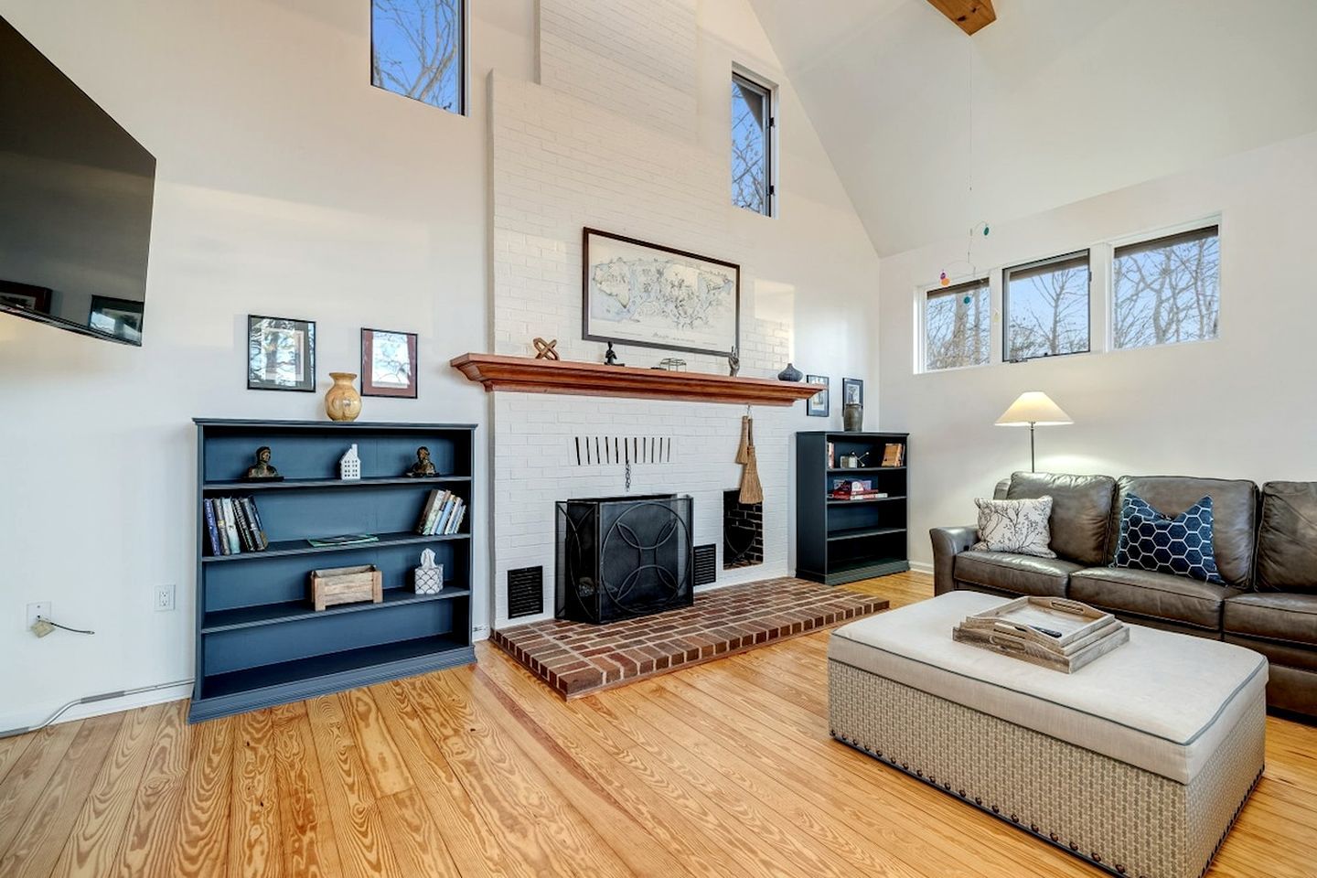 A spacious living room with a fireplace, wooden flooring, a sofa, and a bookshelf.