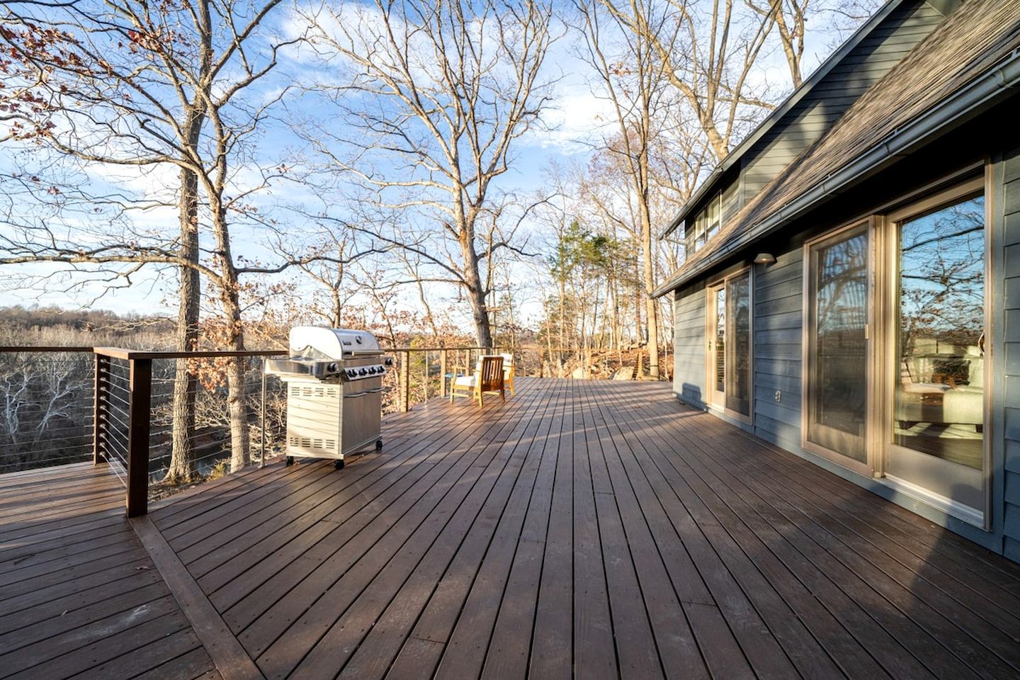 A deck with a grill, a chair, and a building with large windows.
