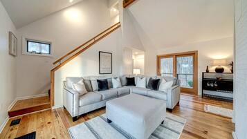 A modern living room with a sectional sofa, wooden flooring, and a staircase.