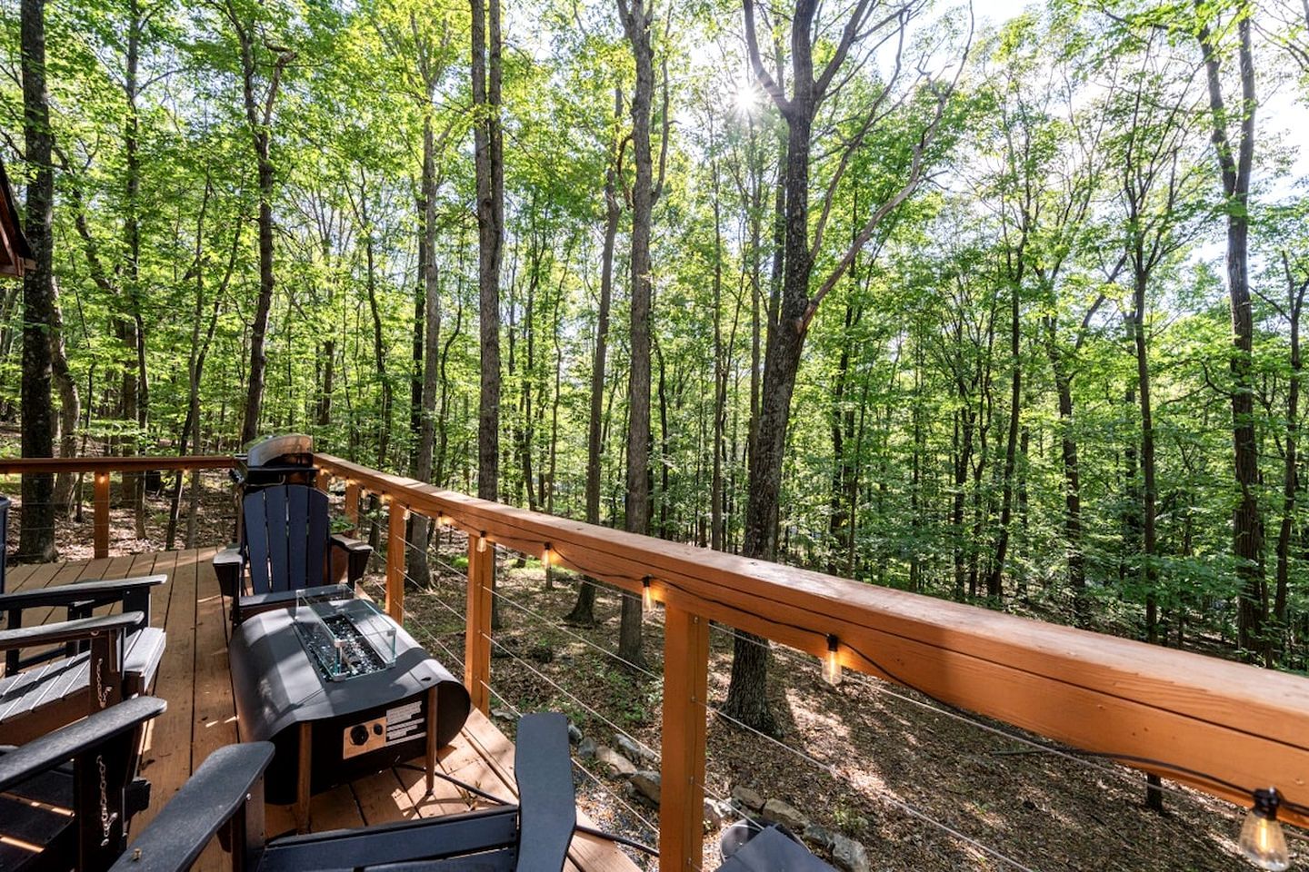 Une terrasse avec coin salon extérieur et barbecue, entourée d’une forêt.