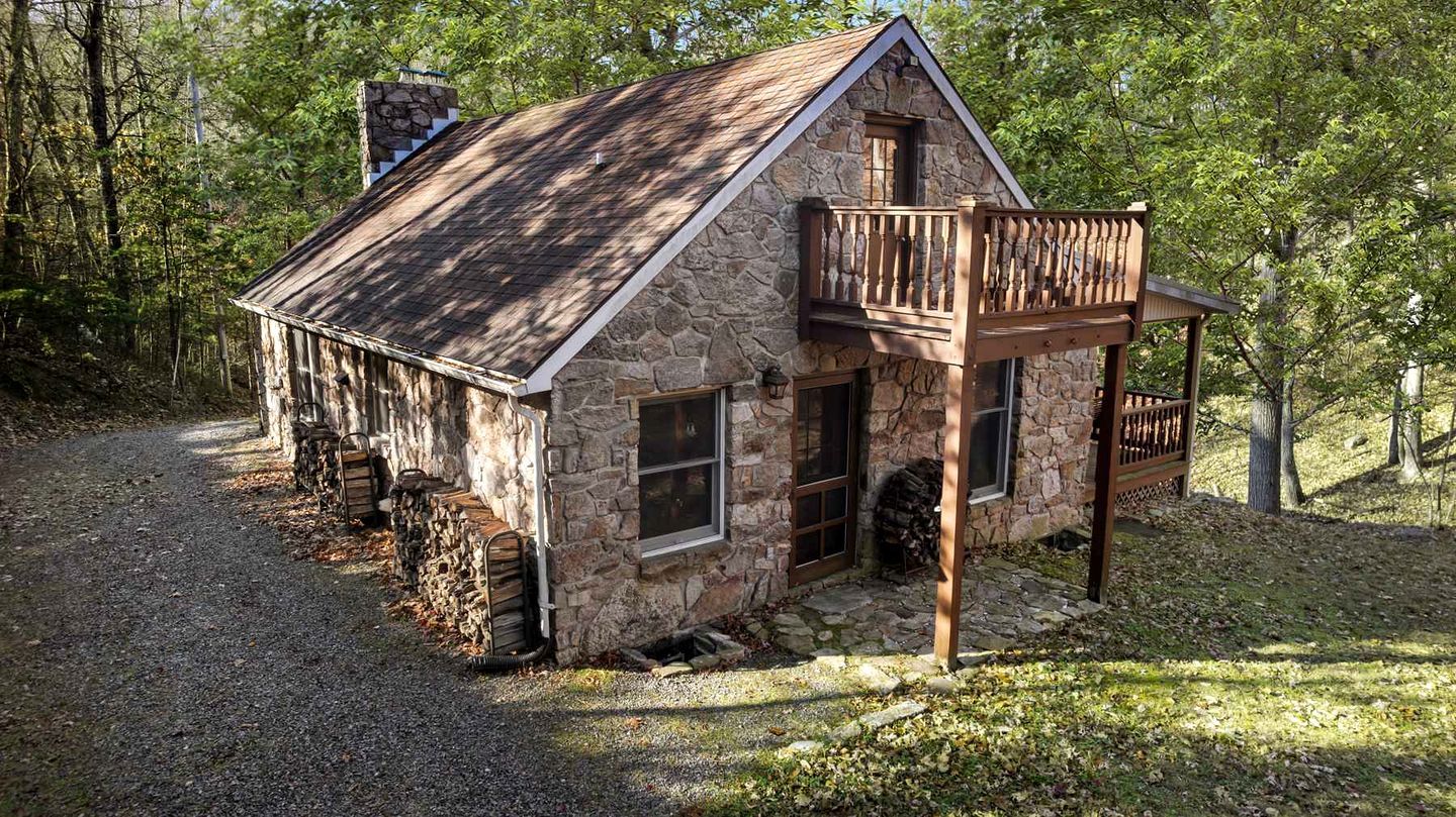 A stone cabin with a wooden balcony, surrounded by trees.