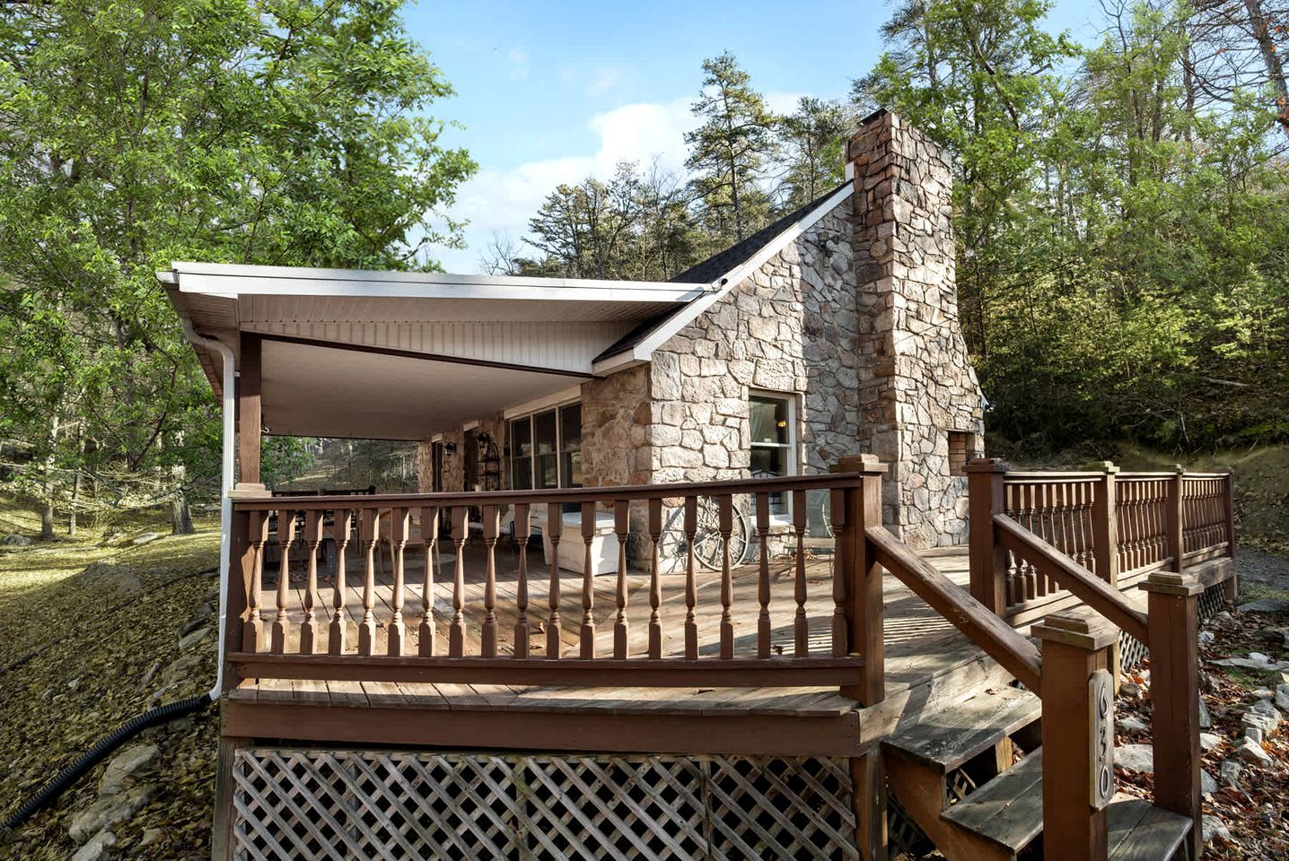 A stone building with a wooden deck and railing, surrounded by trees.