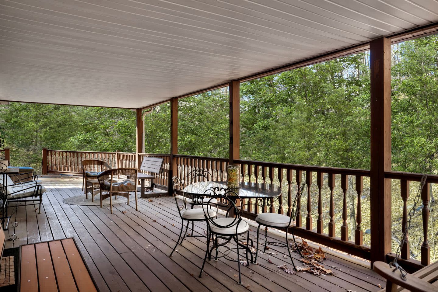 A covered outdoor deck with wooden flooring, metal-framed tables and chairs, and a railing.