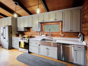 A modern kitchen with grey cabinets, stainless steel appliances, and a wooden ceiling.