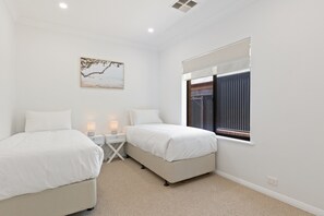 Quarto com duas camas, mesa de cabeceira, abajur, quadro e janela com persianas.