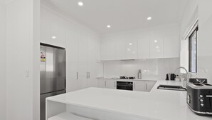 A modern kitchen with white cabinetry, a stainless steel refrigerator, a built-in oven, and a black toaster.