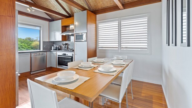 A modern kitchen with wooden beams, white cabinetry, and a dining area with a wooden table set for six. - Beachfront 3-bed With Private Pool & Fireplace (Sunshine Coast)