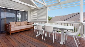 A wooden deck with a white table and chairs, a beige sofa, and a covered area with a white railing. - Beachfront 3-bed With Private Pool & Fireplace (Sunshine Coast)