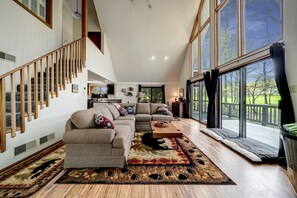 A spacious living room with a large window, a staircase, and a cozy seating area.