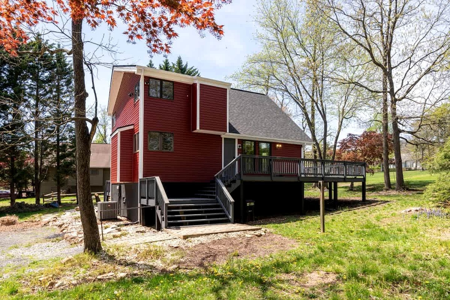 A red two-story house with a deck and stairs leading to a covered porch.