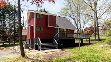 A red two-story house with a deck and stairs leading to a covered porch.
