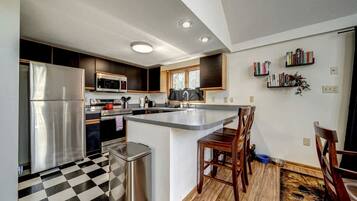A modern kitchen with a stainless steel refrigerator, microwave, and oven, a checkered floor, and a small dining area with a wooden table and chairs.