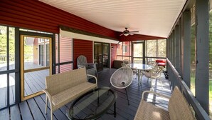 Une véranda couverte, meublée de meubles en osier, avec une table en verre et un ventilateur de plafond.