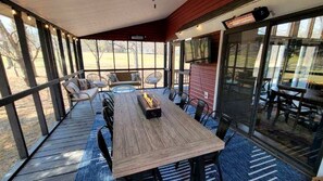 A covered outdoor dining area with a wooden table and chairs, a fire feature, and a view of the outdoors.